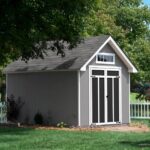 gray 8x12 garden shed surrounded by a white fence, providing a quaint outdoor storage solution